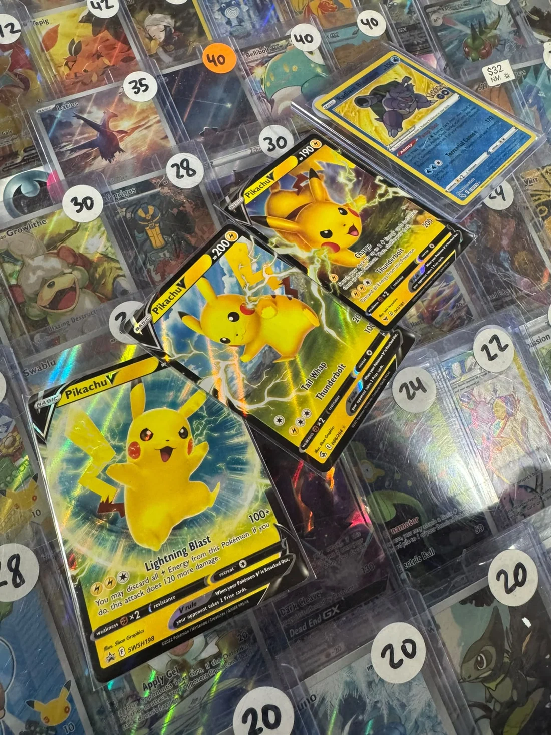 Três Pikachu V de coleções diferentes sobre uma vitrine de cartas com etiquetas de preço